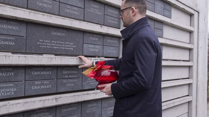 Dyrektor Pawel Bliźniuk zapala znicz przed tabliczką Juliana Grobelnego. 