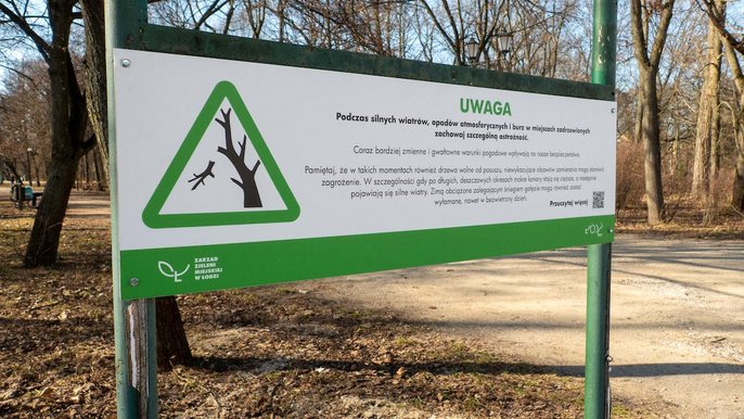 - Tablica informująca o zagrożeniu przy wejściu do parku. Na tablicy grafika trójkąt z zielona obwódką, w środku fragment drzewa z odłamującą się gałęzią. Napis Uwaga, podczas silnych wiatrów zachowaj szczególną ostrożność.