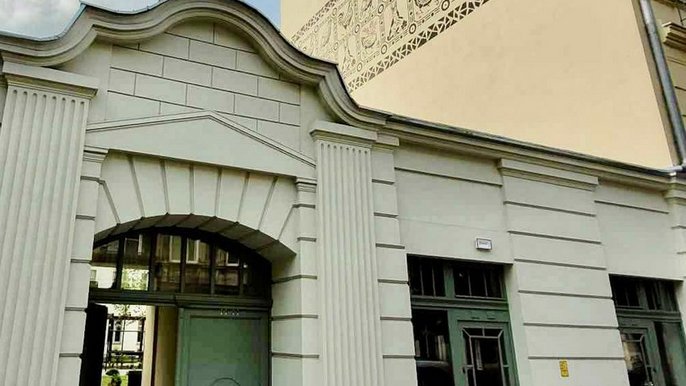 - Zdjęcie przedstawia bramę wejściową do kamienicy w centrum miasta. Na górze napis informujący o spotkaniu konsultacyjnym na prowadzenie świetlicy artystycznej w Łodzi.